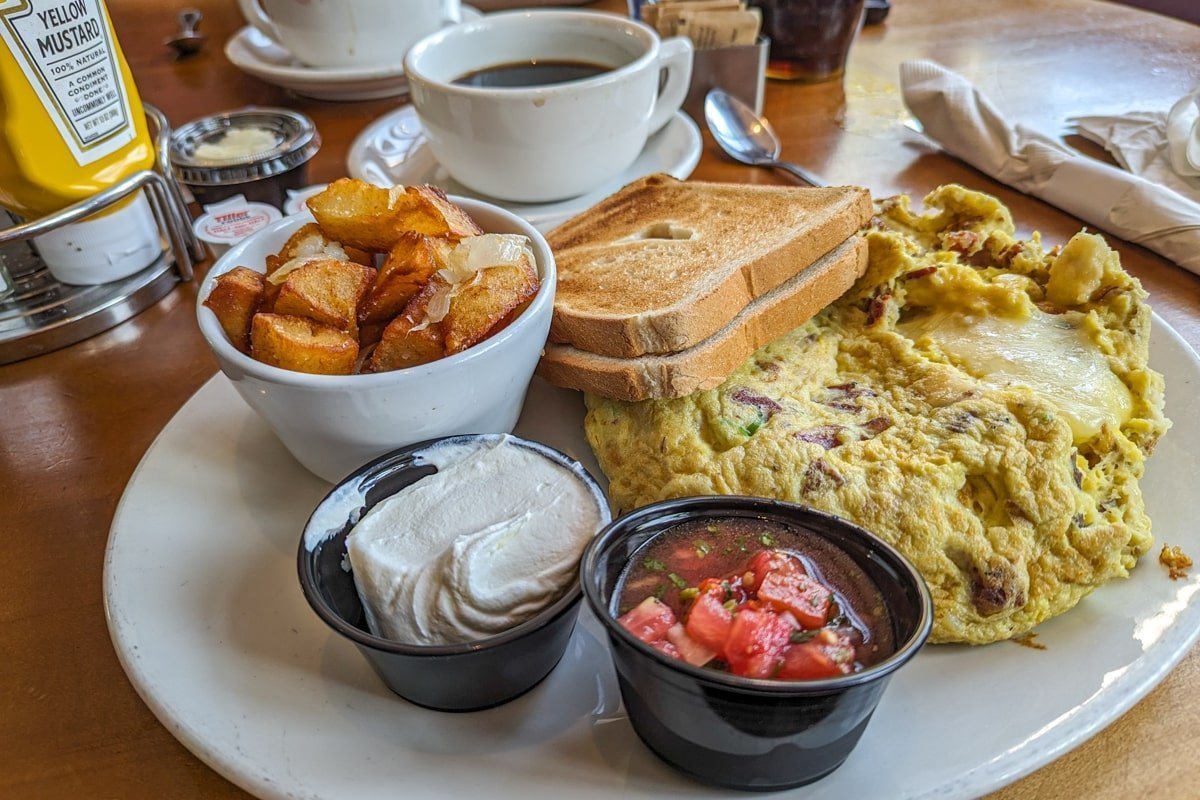Assiette du breakfast avec du café, des tartines grillées, des fruits, des pommes de terre et une omelette